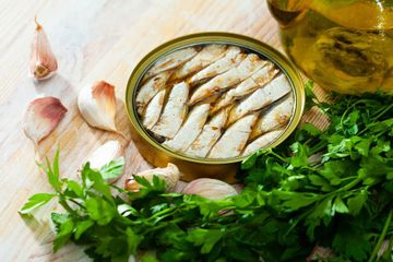 lata de sardinas en conserva sobre una mesa con perejil y dientes de ajo